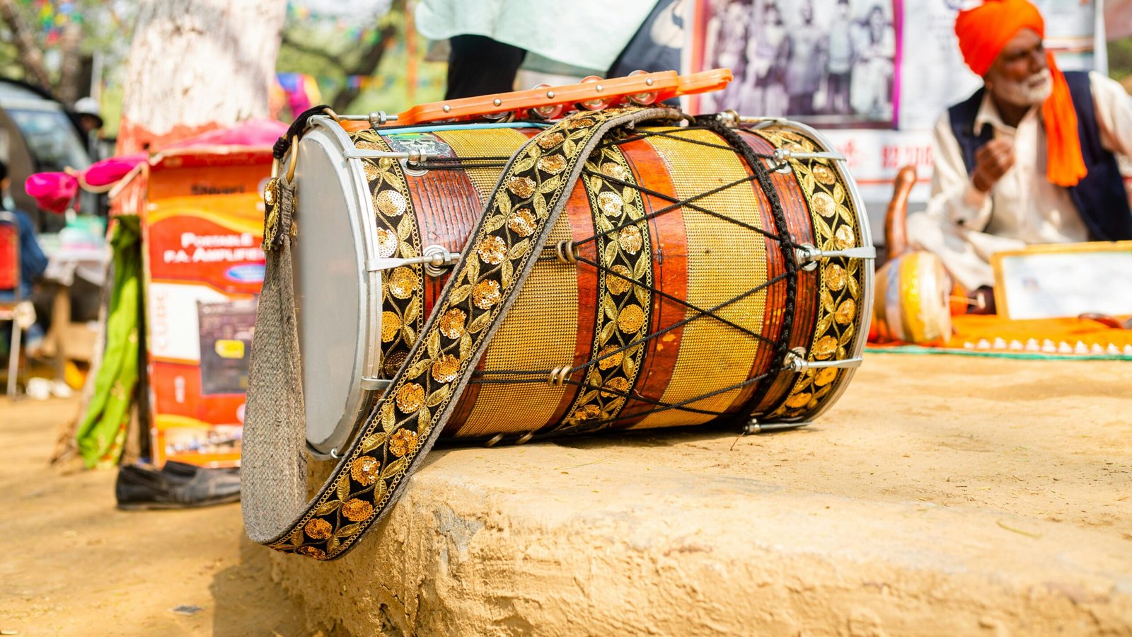 Close-up of a decorated dhol drum at an outdoor cultural event with people in the background.